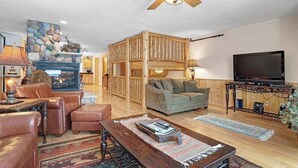 Una sala de estar acogedora con chimenea, televisor, muebles de cuero y un ventilador de techo.