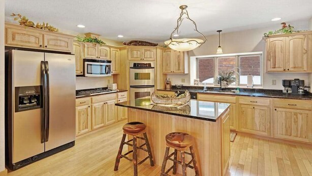 Una cocina moderna con armarios de madera, electrodomésticos de acero inoxidable, una isla central con taburetes y una lámpara colgante.