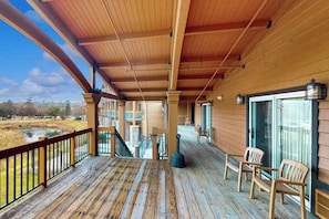 A wooden deck with a railing, a fireplace, and a view of a water body. - Golf-adjacent condo with balcony & arcade (Wisconsin Dells)
