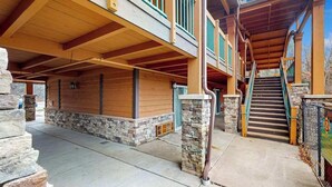 A covered outdoor area with a stone wall, wooden beams, and a staircase leading to an upper level. - Golf-adjacent condo with balcony & arcade (Wisconsin Dells)