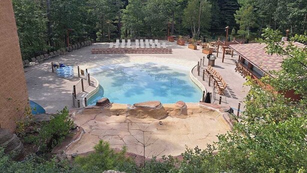 A natural pool surrounded by a wooden deck and stone structures, set in a forested area. - Golf-adjacent condo with balcony & arcade (Wisconsin Dells)