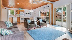 A spacious living area with a wooden ceiling, a kitchen in the background, and a view of a deck. - Inviting lakefront stand-alone condo with private beach, boating, & playground (Wisconsin Dells)