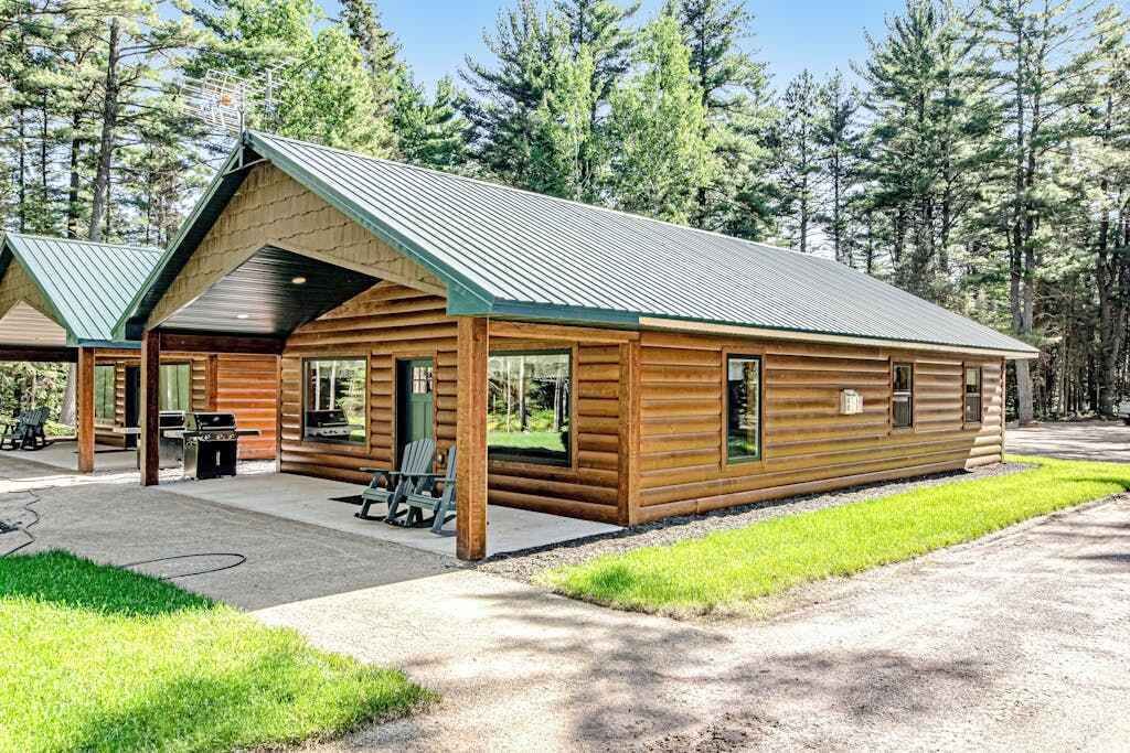 A log cabin with a metal roof, large windows, and a patio area with chairs.