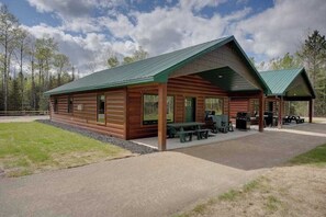 A wooden lodge with a covered patio, picnic tables, and a barbecue area.