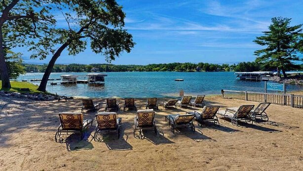 A beach with lounge chairs, a dock, and a lake view. - Ultimate relaxation awaits at Delton Grand Resort on Lake Delton (Wisconsin Dells)