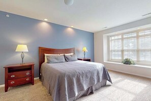Ein Schlafzimmer mit einem Bett, zwei Nachttischen, einem Fenster mit Jalousien und Teppichboden.