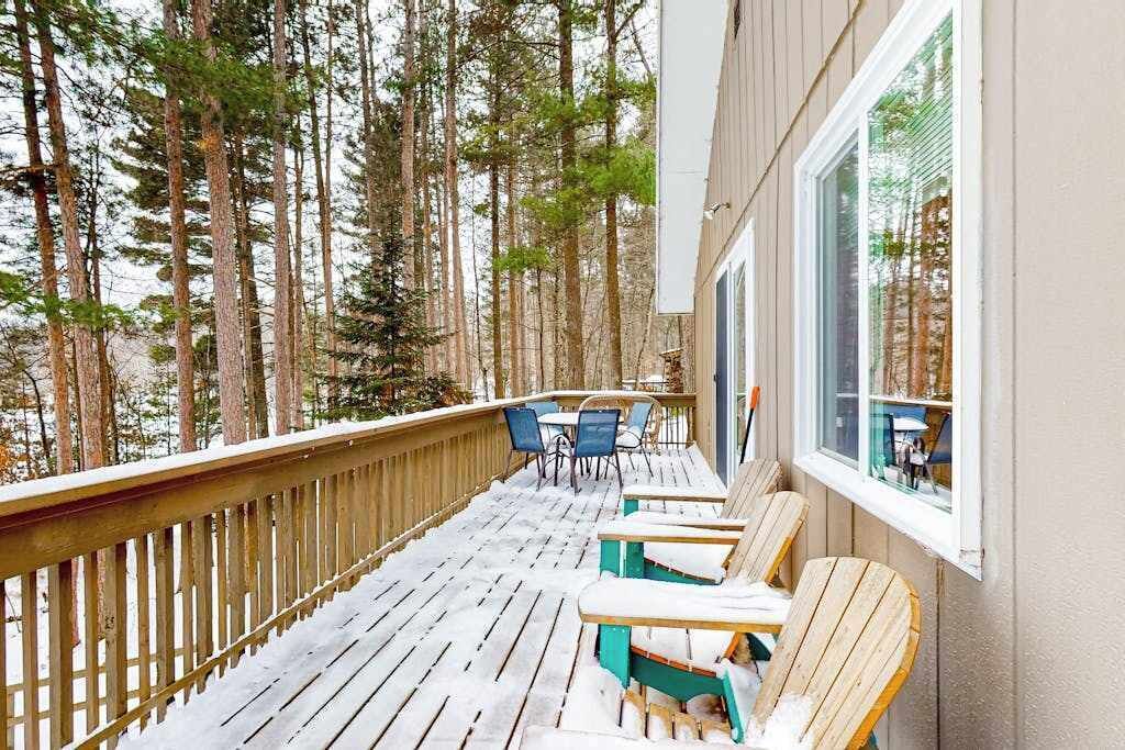 Eine Holzterrasse mit Stühlen und Tisch, umgeben von hohen Bäumen.