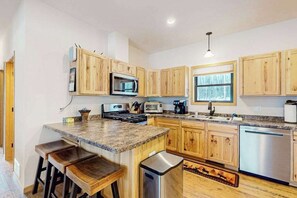 A kitchen with wooden cabinets, a granite countertop, a stainless steel dishwasher, and a built-in microwave. - Lakefront escape on Sugar Maple w/ dock, firepit, kayaks, & gas grill- Dogs-OK (Phelps)