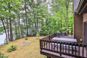 A deck with outdoor seating, surrounded by tall trees and a lake. - Lakefront home with firepit, screened porch, WiFi, central AC, and kayaks (Lac Du Flambeau)