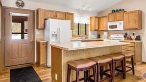 Una cucina con mobili in legno, un frigorifero bianco, un forno a microonde e un angolo con uno sgabello da bar.