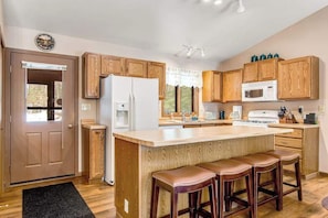 A kitchen with wooden cabinets, a white refrigerator, a microwave, and a bar stool seating area. - Lakefront home with firepit, screened porch, WiFi, central AC, and kayaks (Lac Du Flambeau)