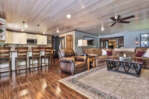 A spacious living area with a wooden ceiling, a kitchen with white cabinets, a bar area, and a seating area with a couch and chairs. - Private waterfront home with dock, kayaks, firepit, & open layout - dog-friendly (Boulder Junction)