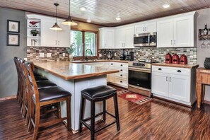 A modern kitchen with white cabinets, a central island with stools, stainless steel appliances, and a wooden ceiling. - Private waterfront home with dock, kayaks, firepit, & open layout - dog-friendly (Boulder Junction)