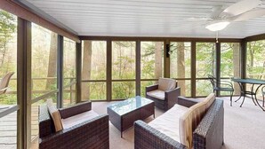 A covered outdoor seating area with wicker furniture and a table, large windows, and a ceiling fan. - Lakefront cabin with kayaks, firepit, dock & spacious interior (Woodruff)