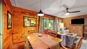 A wooden cabin interior with a dining table, chairs, a sofa, a television, and a ceiling fan. - Lakefront cabin with kayaks, firepit, dock & spacious interior (Woodruff)