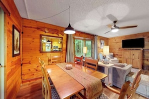 Ein Holzblockhaus-Innenraum mit Esstisch, Stühlen, einer Couch, einem Fernseher und einem Deckenventilator.