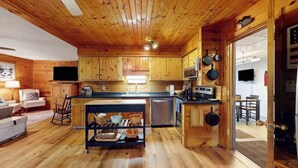 A wooden cabin interior with a kitchen, dining area, and a living space with a sofa and a TV. - Lakefront cabin with kayaks, firepit, dock & spacious interior (Woodruff)