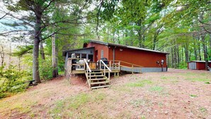 A rustic cabin with a wooden deck and a staircase leading to a porch. - Lakefront cabin with kayaks, firepit, dock & spacious interior (Woodruff)