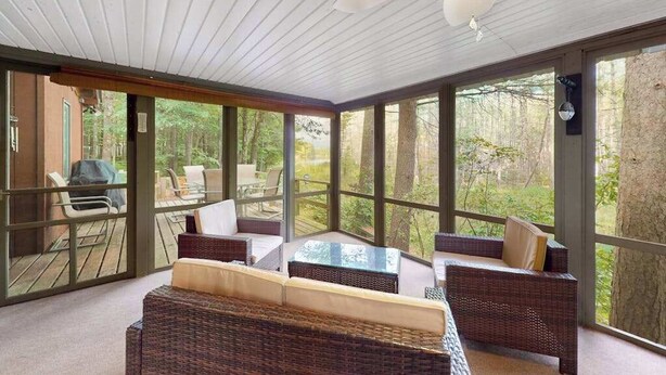 A room with wicker furniture, large windows, and a ceiling fan. - Lakefront cabin with kayaks, firepit, dock & spacious interior (Woodruff)