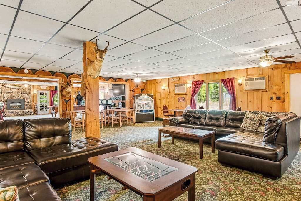A cozy lodge interior with a fireplace, leather sofas, and a wooden ceiling.
