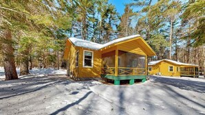 A cabin with a porch, surrounded by snow and trees. - Lakeview cabin with dock access, kayaks, row boat, firepit & year-round fun (St. Germain)