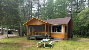 A cabin with a porch, a chimney, and a picnic table in a wooded area. - Lakeview cabin with dock access, kayaks, row boat, firepit & year-round fun (St. Germain)