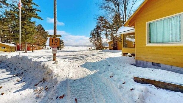 A snow-covered road with a speed limit sign, a yellow building with a window, and a clear sky. - Lakeview cabin with dock access, kayaks, row boat, firepit & year-round fun (St. Germain)