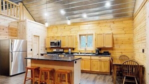 Una cucina funzionale con mobili in legno, frigorifero in acciaio inossidabile, microonde e macchina da caffè. Sono presenti sgabelli di legno all'isola della cucina.