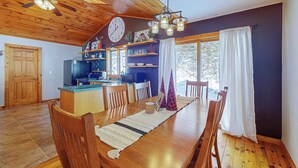 A wooden interior with a dining table, chairs, a kitchen area, and a large window. - Serene Home w/ large fenced in yard, jetted tub, WIFI, near Lakes & Trails (St. Germain)