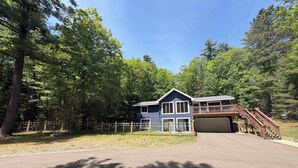 A two-story building with a garage, surrounded by a wooden fence and trees. - Serene Home w/ large fenced in yard, jetted tub, WIFI, near Lakes & Trails (St. Germain)