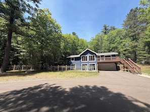 A two-story building with a garage, surrounded by a wooden fence and trees. - Serene Home w/ large fenced in yard, jetted tub, WIFI, near Lakes & Trails (St. Germain)