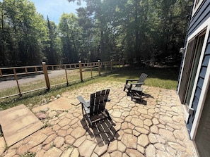 A patio with hexagonal stone tiles, two Adirondack chairs, and a wooden fence. - Serene Home w/ large fenced in yard, jetted tub, WIFI, near Lakes & Trails (St. Germain)