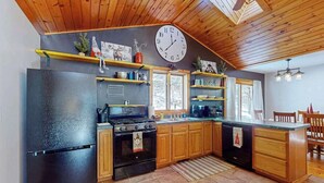 A kitchen with wooden cabinets, a black refrigerator, a stove, and a clock on the wall. - Serene Home w/ large fenced in yard, jetted tub, WIFI, near Lakes & Trails (St. Germain)