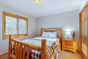 Quarto com cama de madeira, mesa de cabeceira com abajur e guarda-roupa.