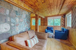 A wooden cabin interior with a stone wall, a brown leather sofa, and blue chairs. - Dog-friendly lakefront home with boat access, deck, fireplace, gas grill, kayaks (Winchester)