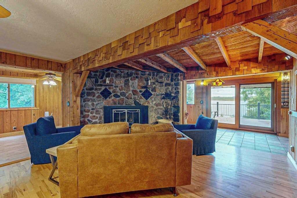 A spacious living area with a stone fireplace, wooden ceiling beams, and large windows.