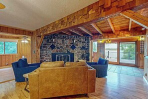 A spacious living area with a stone fireplace, wooden ceiling beams, and large windows. - Dog-friendly lakefront home with boat access, deck, fireplace, gas grill, kayaks (Winchester)