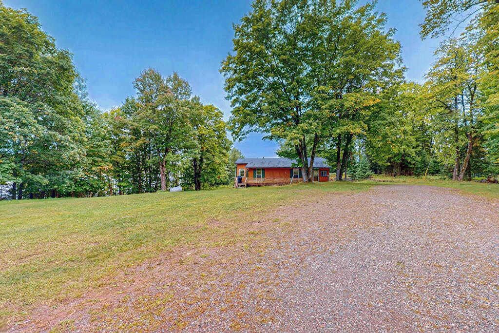 A house with a gravel driveway, surrounded by trees and a grassy area.