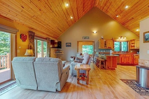 A cozy cabin interior with a living room, kitchen, and dining area, featuring wooden ceilings and large windows. - Beautiful Lakefront Cabin with a Private Dock, Firepit, and Large Yard! (Presque Isle)