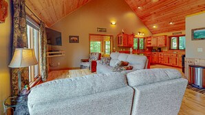 Interior acolhedor de uma cabana, com sala de estar, cozinha e mesa de jantar.