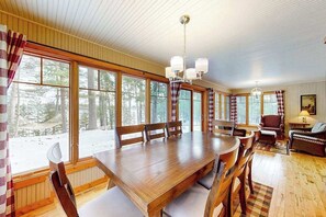 A wooden dining table with chairs, large windows, and a chandelier.