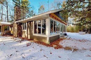 A modern cabin with large windows, a stone chimney, and a wooden deck.