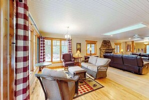 A cozy living room with wicker furniture, a stone fireplace, and large windows.
