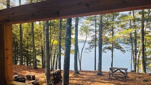 A wooden deck with a bench overlooking a forested area and a lake. - Dog-friendly, lakefront getaway with a firepit, dock, washer/dryer, & AC (St. Germain)