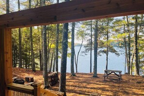 A wooden deck with a bench overlooking a forested area and a lake.