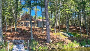 A cabin in a forest with a dock leading to a pond. - Dog-friendly, lakefront getaway with a firepit, dock, washer/dryer, & AC (St. Germain)