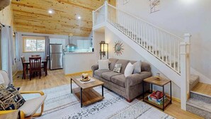 A cozy interior with a wooden ceiling, a staircase, a sofa, a dining area, and a kitchen. - Dog-friendly, lakefront getaway with a firepit, dock, washer/dryer, & AC (St. Germain)