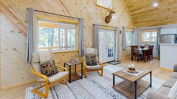 A log cabin interior with a dining area, two rocking chairs, a coffee table, and a deer head mounted on the wall. - Dog-friendly, lakefront getaway with a firepit, dock, washer/dryer, & AC (St. Germain)