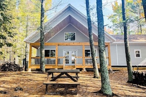 A cabin with a wooden deck, a picnic table, and a forested backdrop.