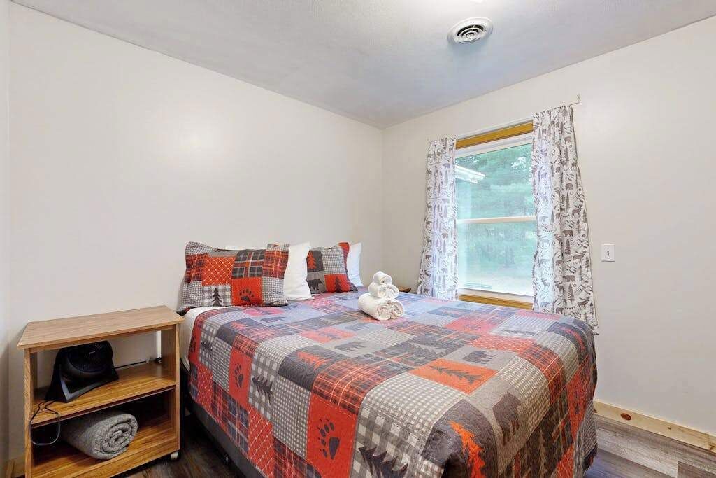 A bedroom with a bed, a nightstand, a window with curtains, and a view of trees outside.